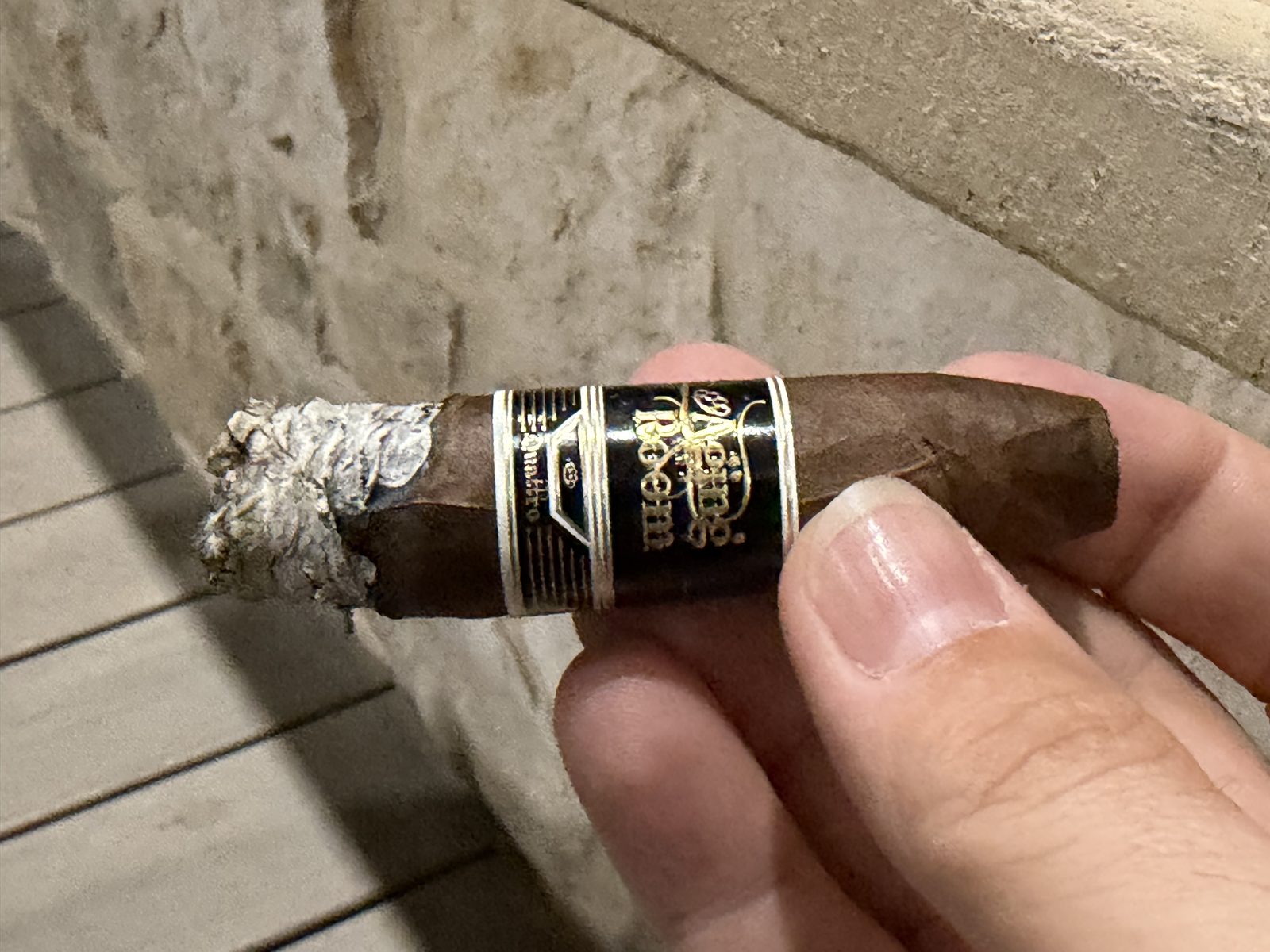 Aging Room Quattro Nicaragua Maestro at the start of the final third with the secondary band off and the main black and gold band still on, a short uneven gray ash at the foot