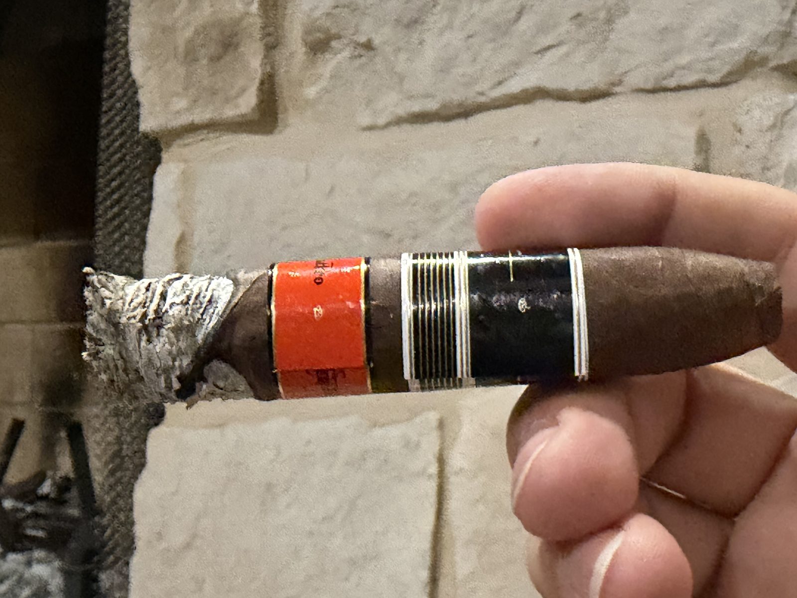 Side view of the Aging Room Quattro Nicaragua Maestro in the second third with a ragged gray ash and a wavy burn line running up toward the orange secondary band