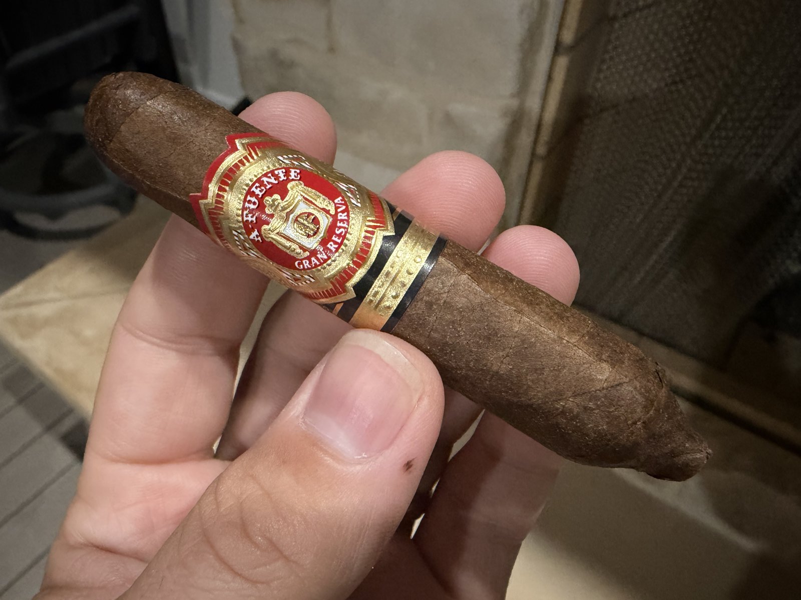 Unlit Arturo Fuente Hemingway Short Story held in hand, medium brown Cameroon wrapper, red and gold A. Fuente Gran Reserva band, tapered perfecto foot