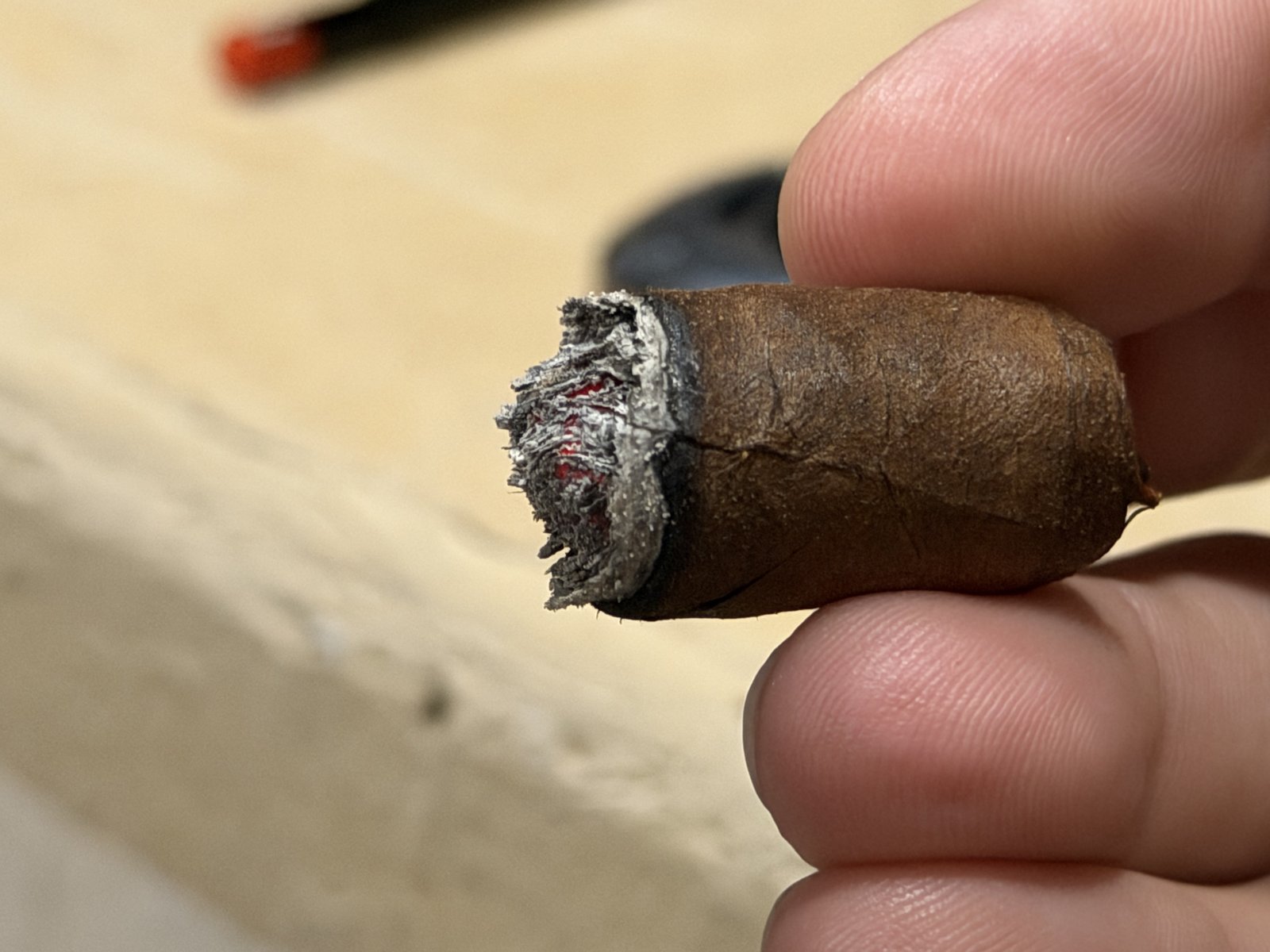 Arturo Fuente Hemingway Short Story nub held between fingers, about three quarters of an inch left, ash freshly knocked off showing the ember