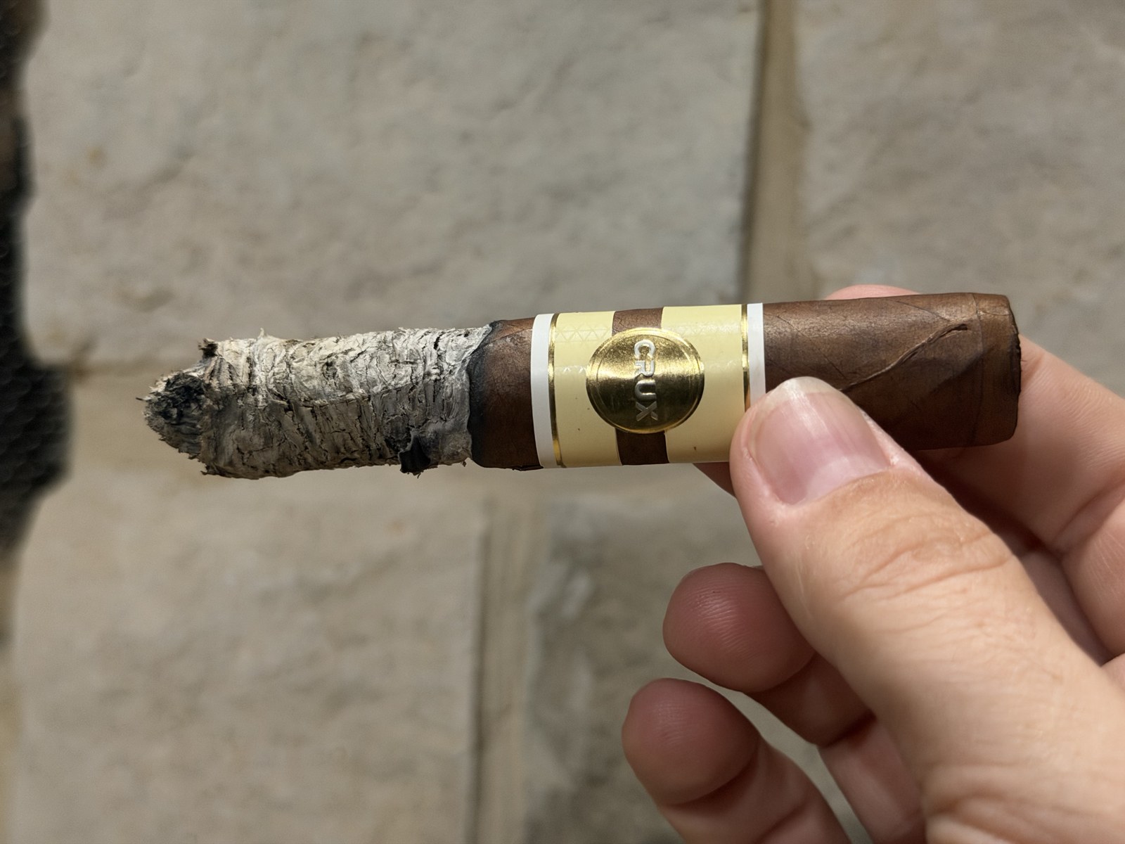 Crux Epicure Habano Toro with a long stacked gray ash and a slightly wavy burn line, gold Crux medallion band visible