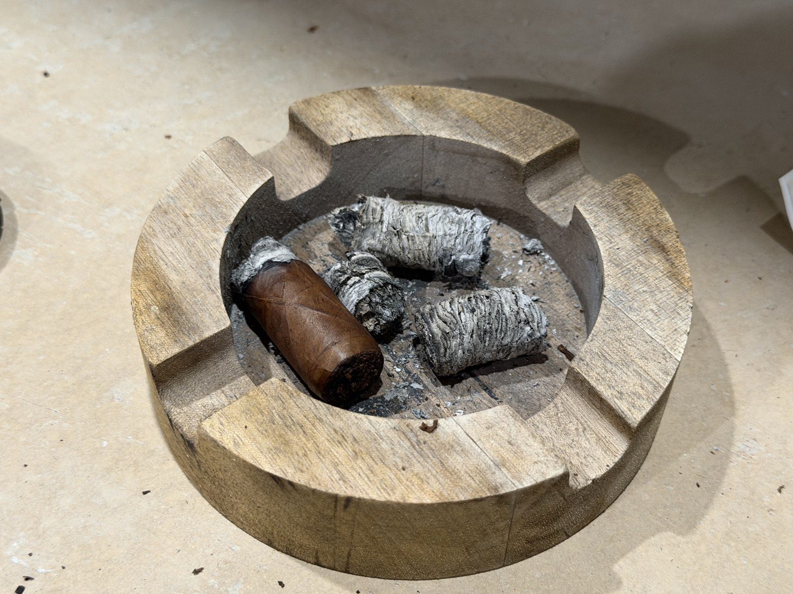 The Crux Epicure Habano Toro nub in a wooden ashtray alongside three intact cylinders of gray ash
