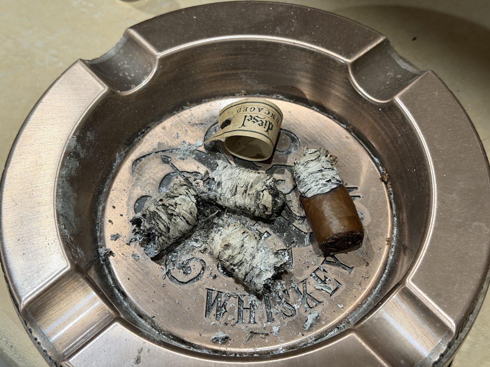 The finished Diesel Uncaged Toro in a copper ashtray: the nub, the ash chunks, and the curled paper Diesel Uncaged band