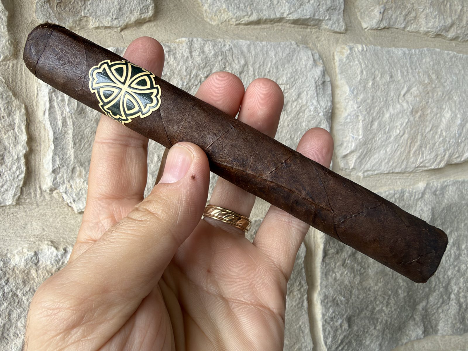 Unlit Dunbarton Sin Compromiso Seleccion No. 7 held in hand against a stone wall, a long dark rustic San Andres wrapper with a soft box press and the black and gold Dunbarton cross band