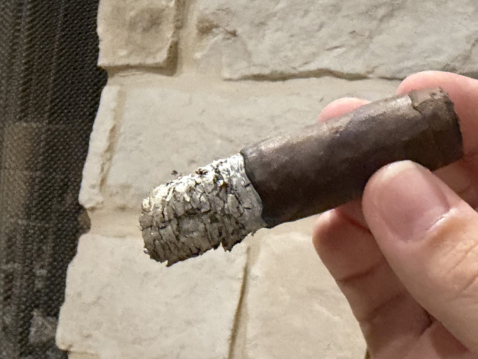The El Rey del Mundo Oscuro Robusto Larga where I put it down about halfway through the final third, bands removed, held between two fingers in front of a stone fireplace with gray ash on the foot