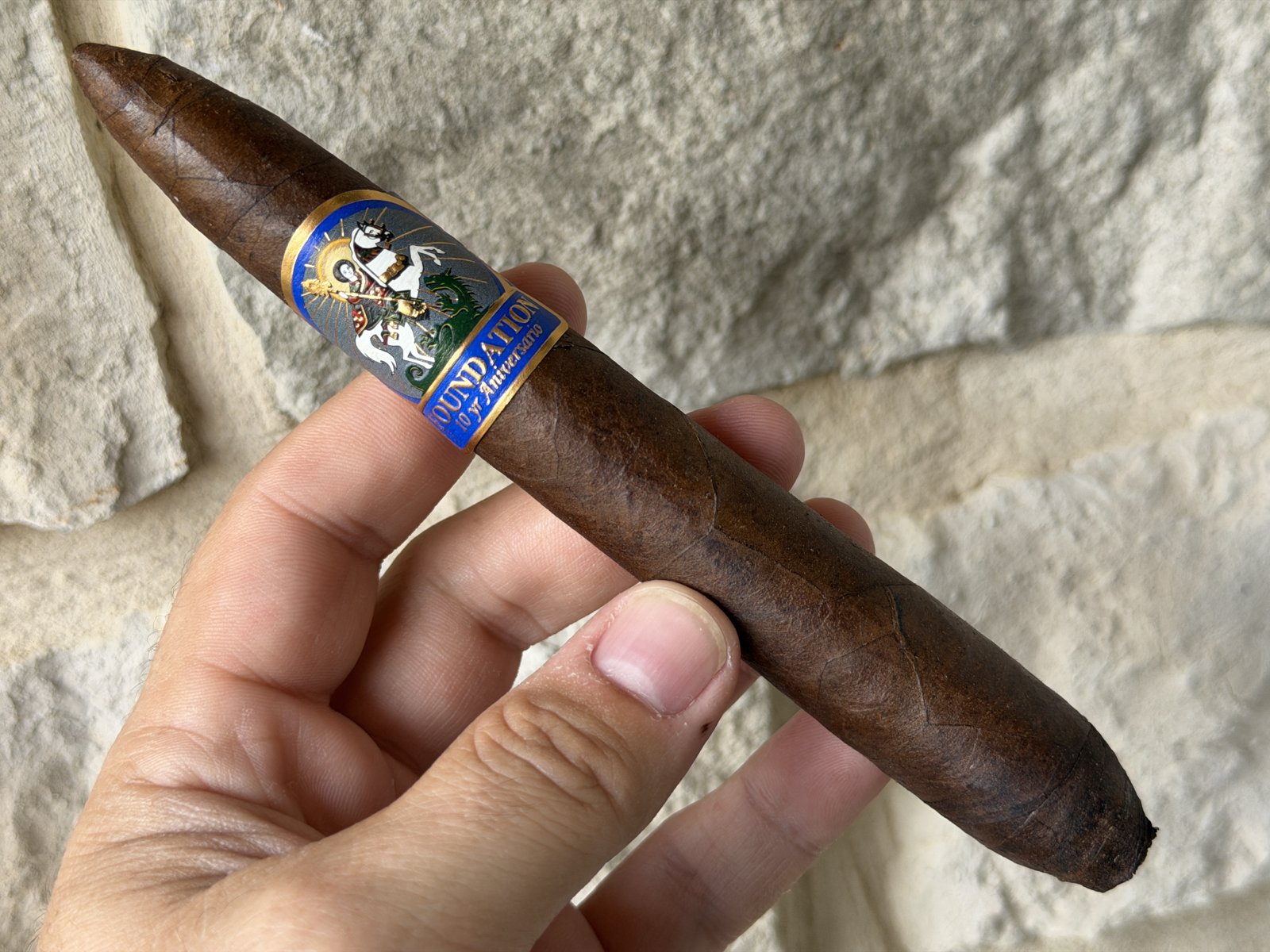 Foundation 10 Year Aniversario Salomon held in hand before lighting, dark rustic wrapper with the blue and gold St. George band