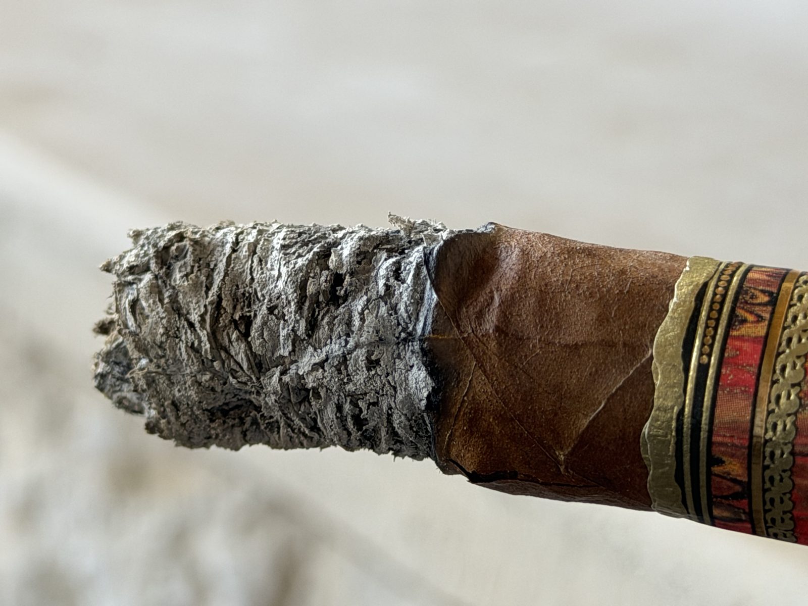 Close-up of the pitted, flaky gray ash on the Fuente Fuente Opus X Perfecxion X during the second third, with the wrapper edge lifting near a crack above the burn line