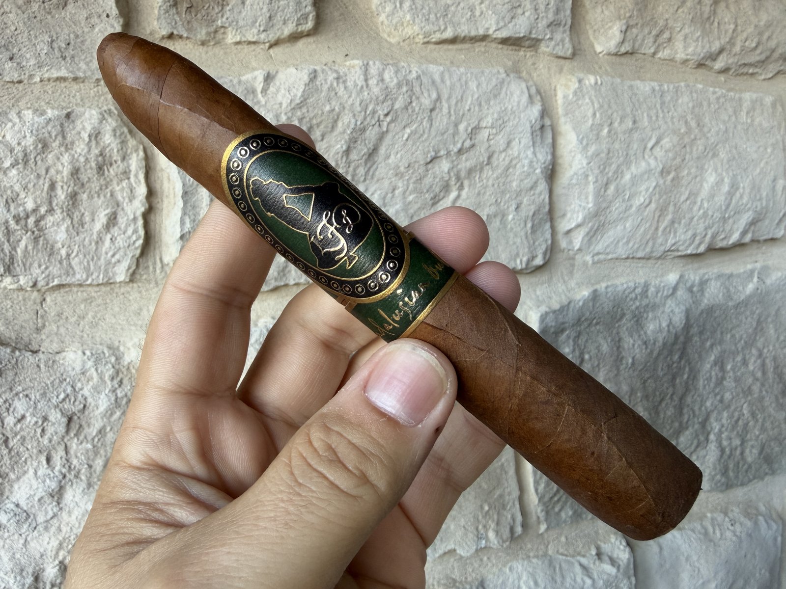 Unlit La Flor Dominicana Andalusian Bull held in hand against a white stone wall, light brown wrapper with the green and gold LFD band and Andalusian Bull secondary band