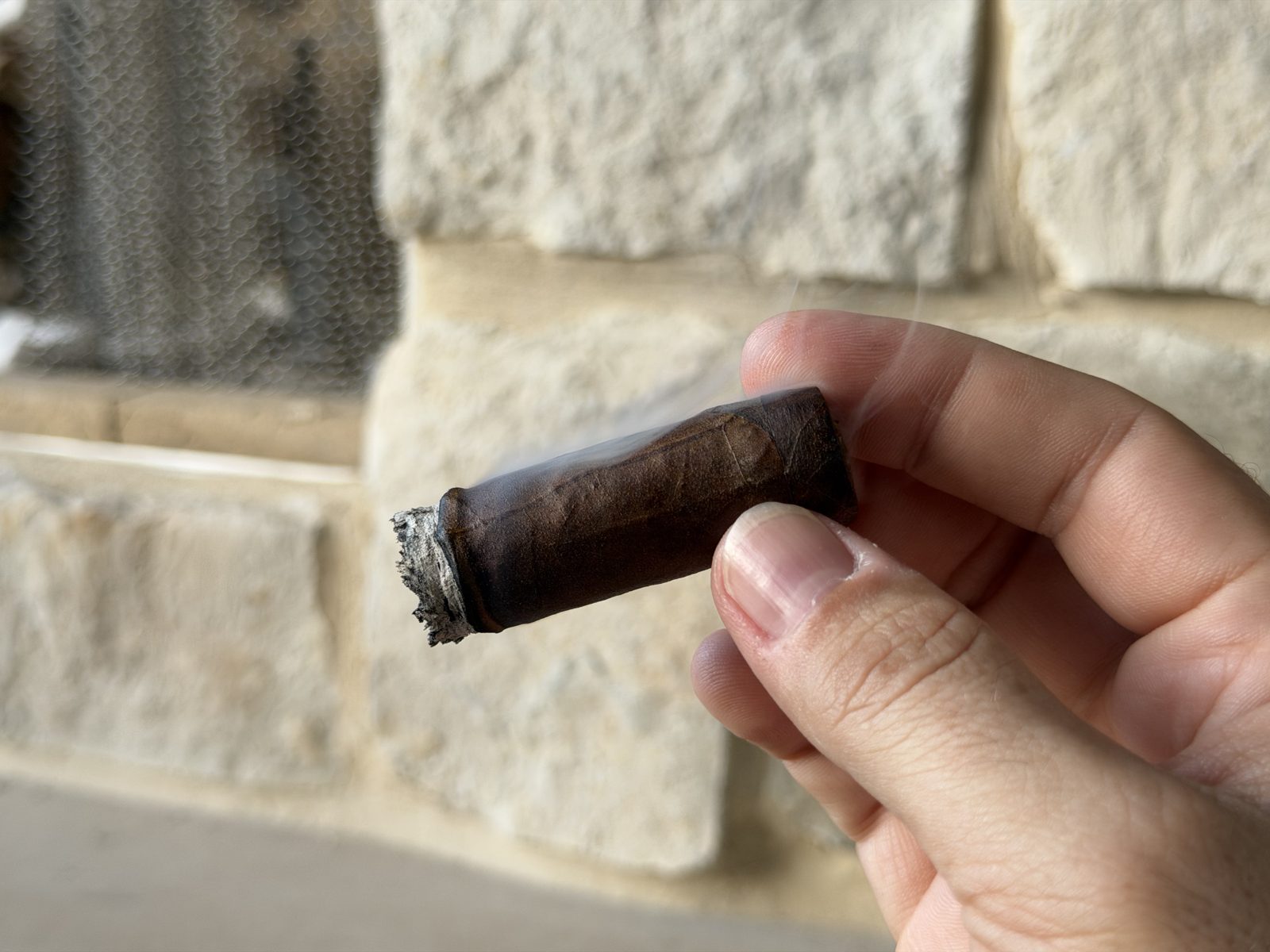 The Liga Privada No. 9 Toro in the final third held between fingers against a stone wall, freshly relit after going out