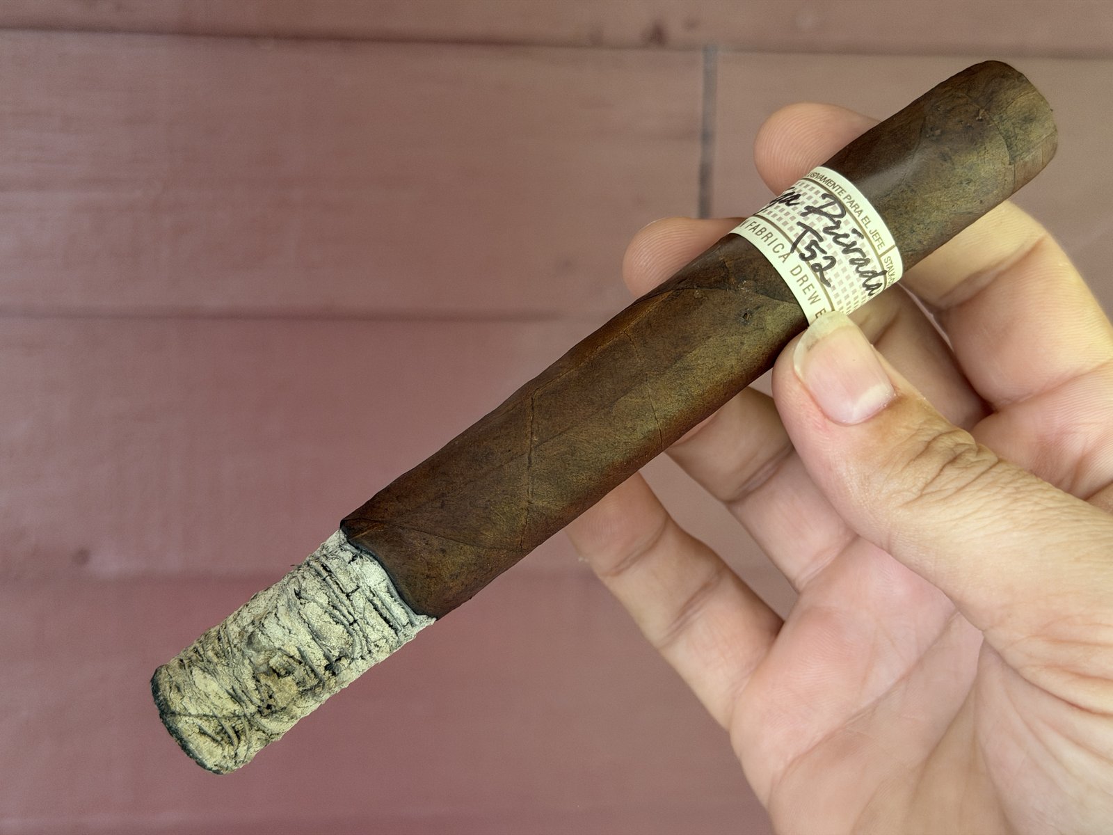 Long, tight, light-gray stacked ash on the lit Liga Privada T52 with the band still on, held against a painted wall