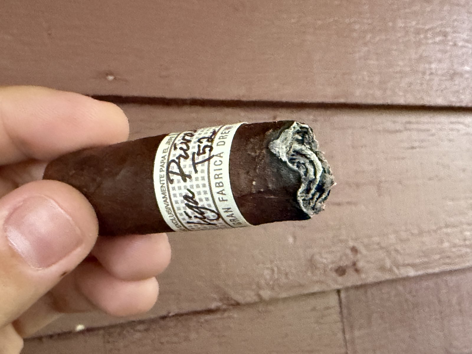 Liga Privada T52 burned down into the final third, band still on, ash at the foot, held against a wood wall