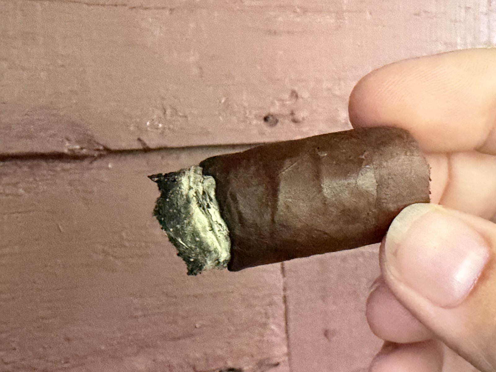 Liga Privada T52 smoked down near the end, short and held against a painted wall, loose greenish-gray ash at the foot