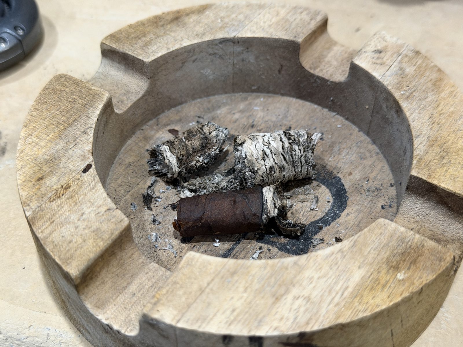 Round wooden ashtray holding the Nasty Fritas nub and two long segments of gray and white ash