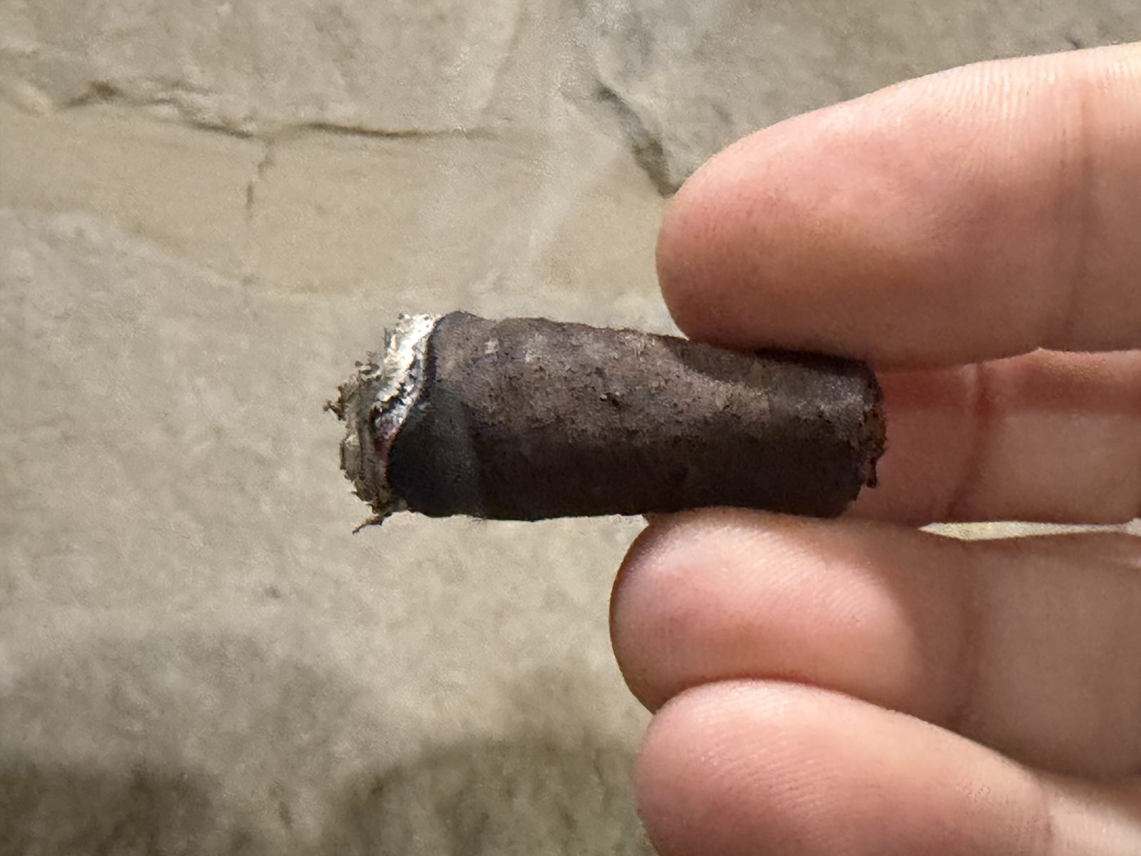 Short nub of the Liga Privada Unico Serie Nasty Fritas, about an inch of dark wrapper with a thin burned edge, held in fingertips
