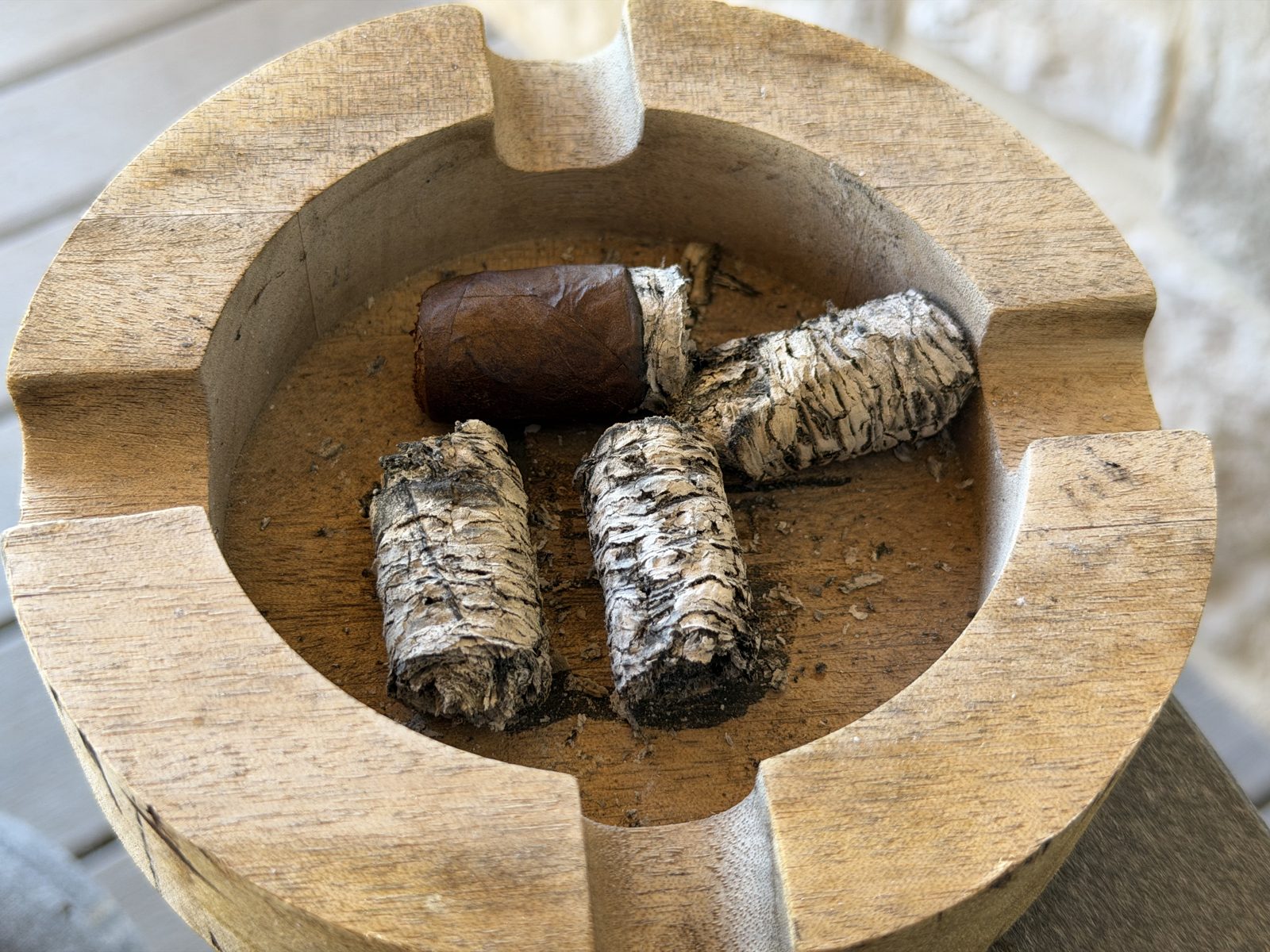 Wooden ashtray holding the Liga Undercrown Maduro Gran Toro nub and three solid cylinders of layered gray and white ash