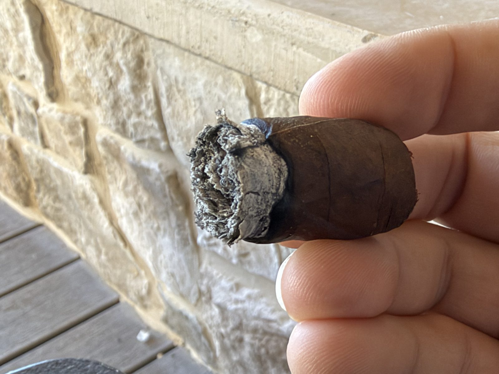 Close-up of the Liga Undercrown Maduro Gran Toro nub just after the final ash came off, with a slightly concave center at the foot, held over a wooden deck