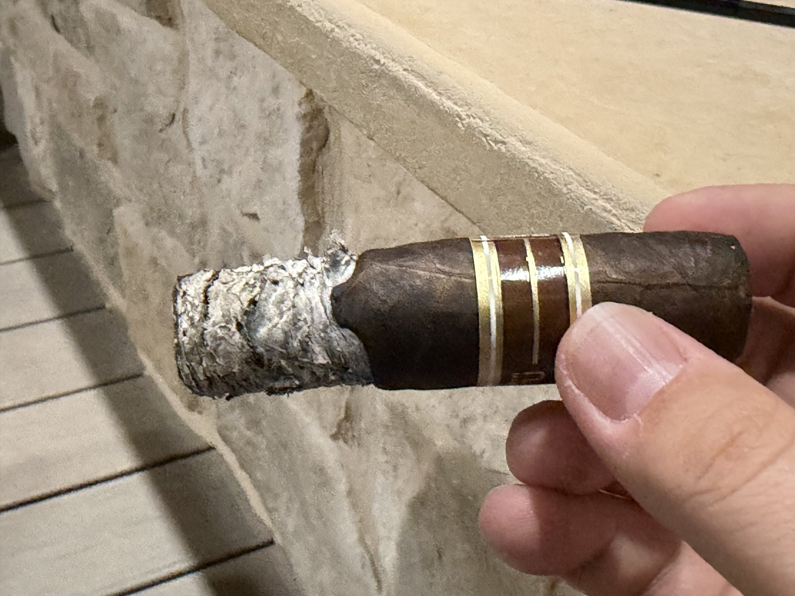 Nub Maduro 460 resting on a stone ledge with a long, flaky, crumbling ash still attached