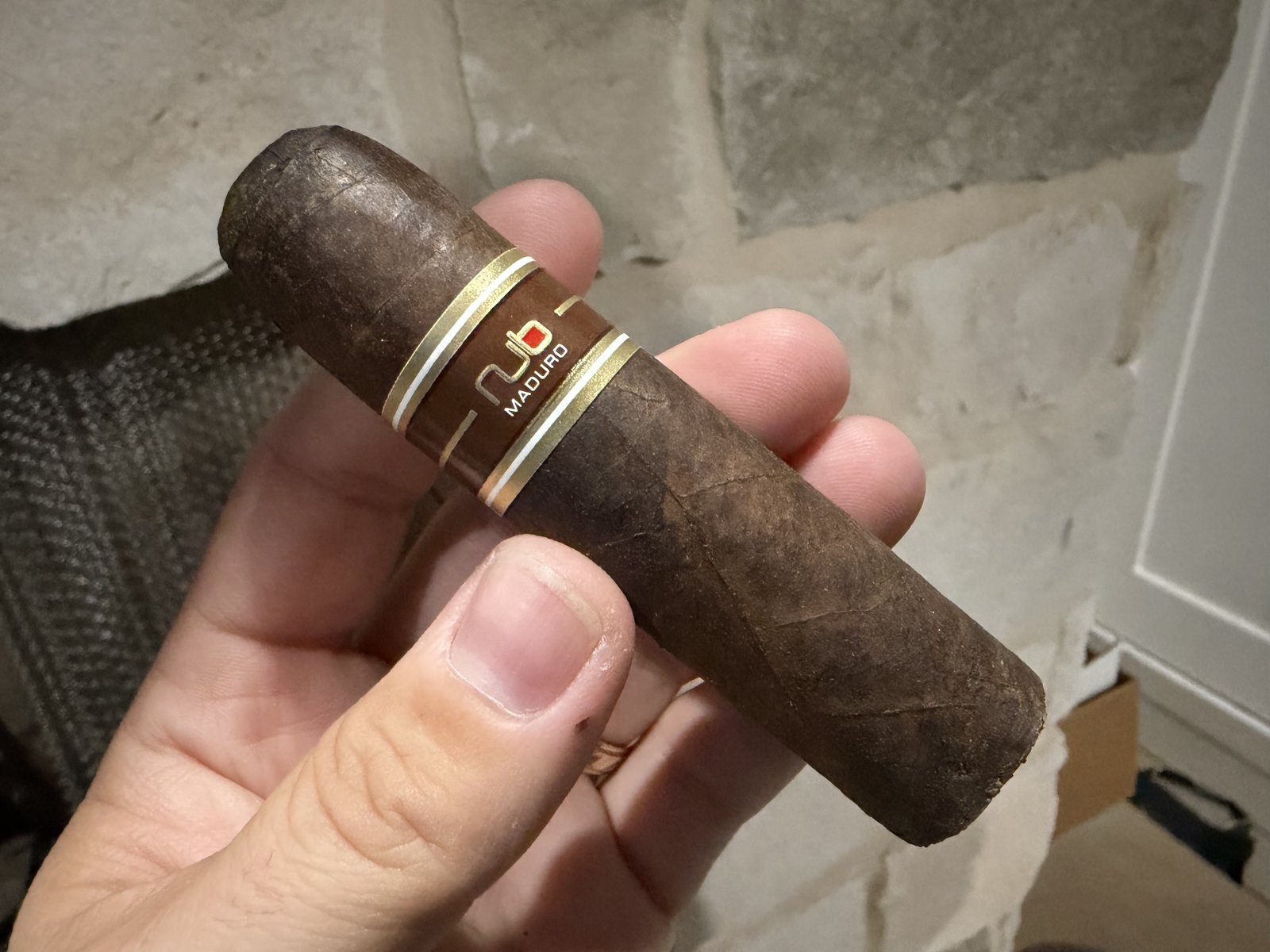 Unlit Nub Maduro 460 held in hand, short fat dark-brown San Andrés wrapper with the brown-and-gold Nub Maduro band