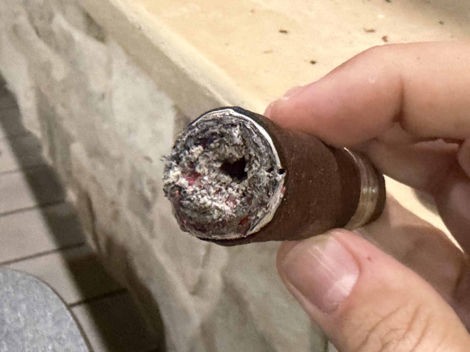 Close-up of the foot of the Oliva Master Blends 3 Churchill at the end of the first third, ash knocked off, showing a hole off center in the lit filler, held in fingertips