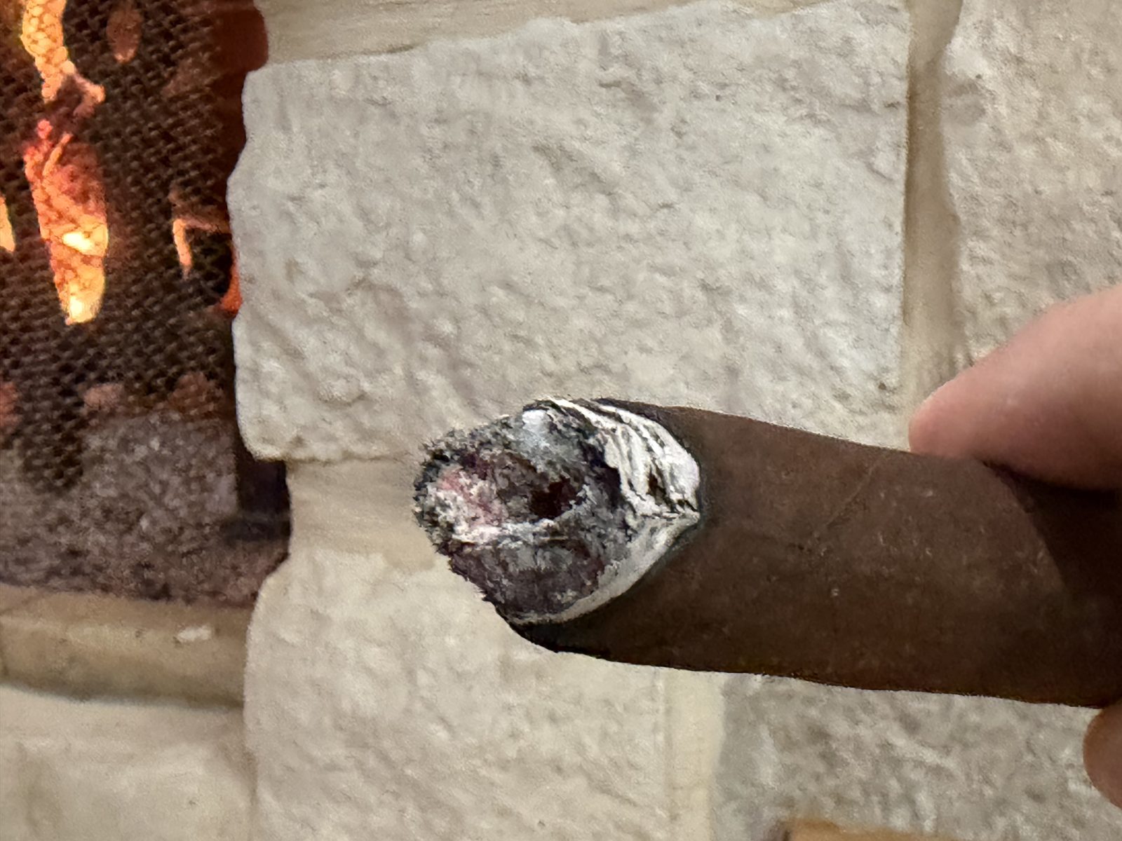 Foot of the Oliva Master Blends 3 Churchill after ashing, showing the glowing cherry with a dark hole burned into the upper part of the center, held against a stone wall
