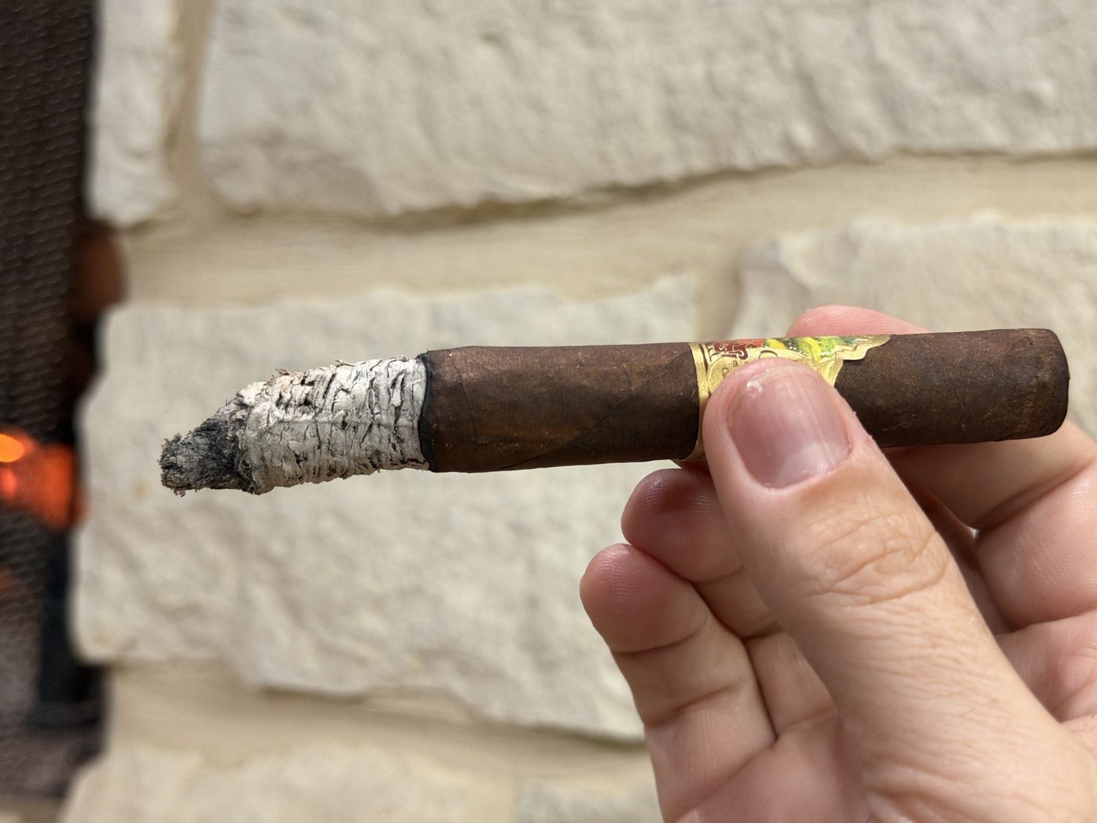 Oliva Master Blends 3 Churchill in the second third with a long white ash and the band still on, held in hand against a stone wall