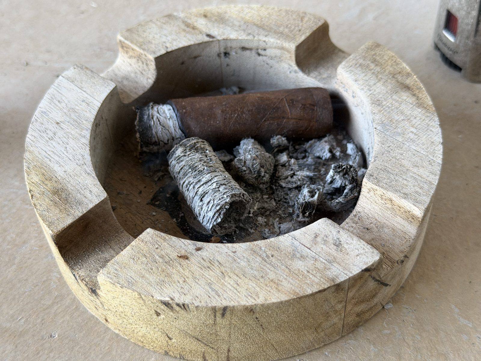 Wooden ashtray holding the Oliva Serie V Maduro Toro laid down with a short ash on the foot, next to a cylinder of layered gray ash and loose ash pieces