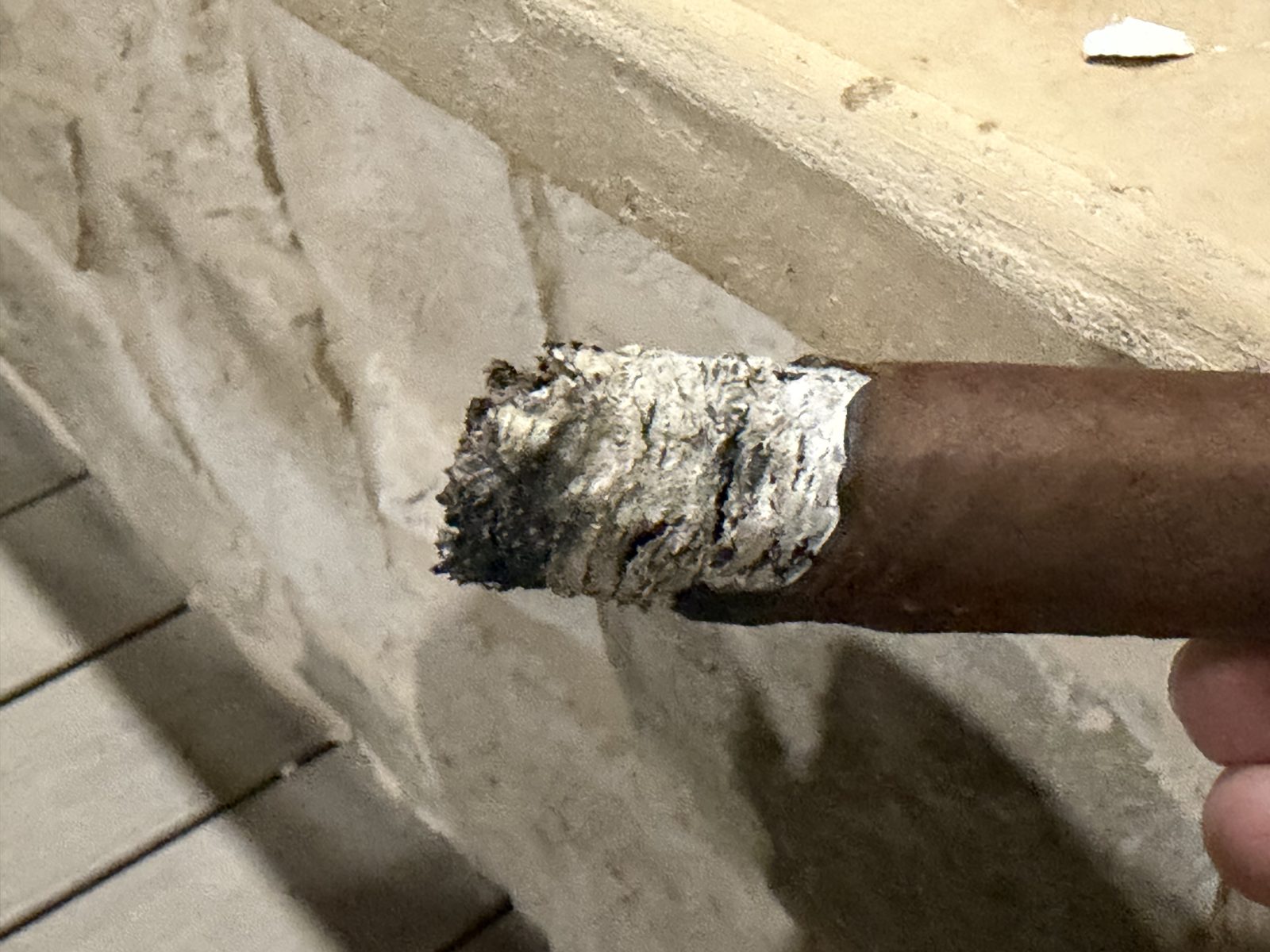 Close-up of the Perdomo 30th Anniversary Maduro Epicure in the second third, a ragged gray ash with the burn line sitting about half an inch higher on one side than the other