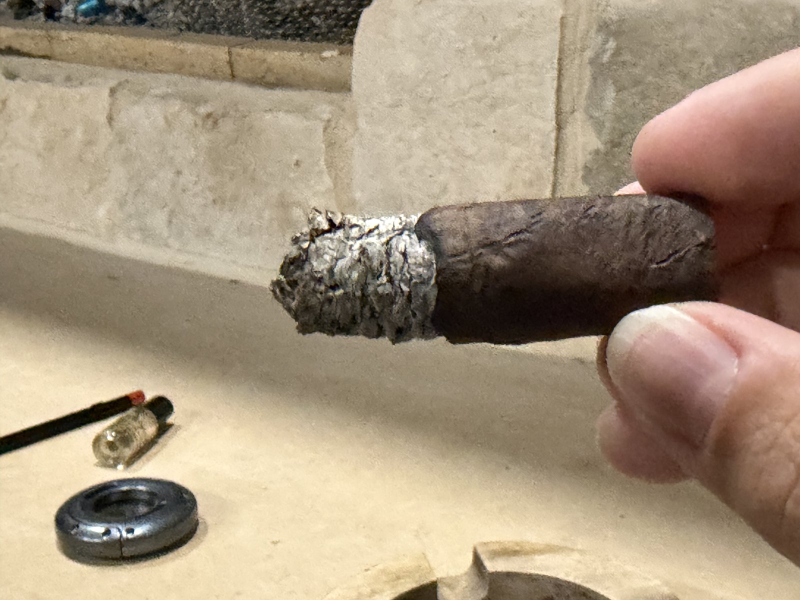 The La Historia Doña Elena at the end of the smoke, held in hand with a short flaky ash, cutter and lighter on the stone ledge behind