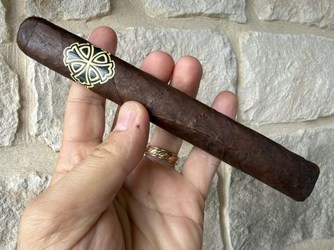 Unlit Dunbarton Sin Compromiso Seleccion No. 7 held in hand against a stone wall, a long dark rustic San Andres wrapper with a soft box press and the black and gold Dunbarton cross band